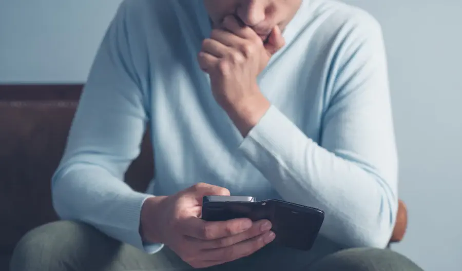 A young man is sitting on an old antique sofa and is using a smart phone